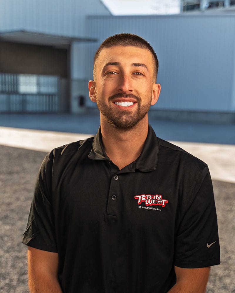 Man smiling outside industrial building in black shirt.