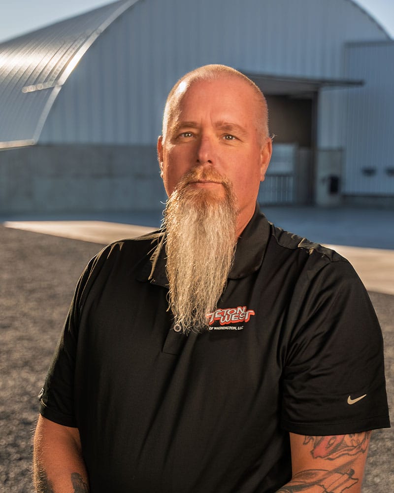 Man with long beard in front of hangar