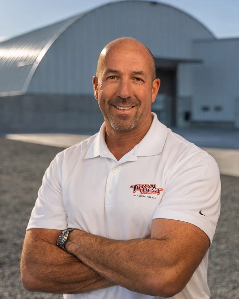 Smiling man in white shirt outside industrial building.